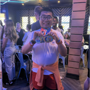 Tommy He poses with his San Francisco Marathon and challenge medals in front of a lively bar.